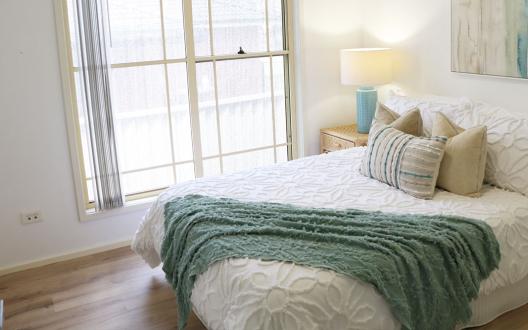a light and airy styled bedroom with a white doona cover and teal green throw and cushions