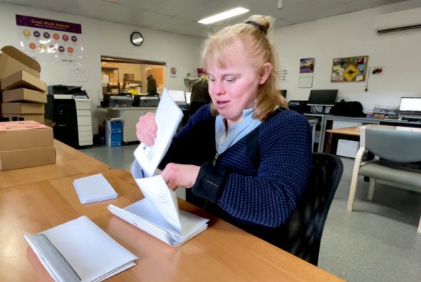 a supported employee sitting at a desk at Unisson's Pack Works folding letters into envelopes
