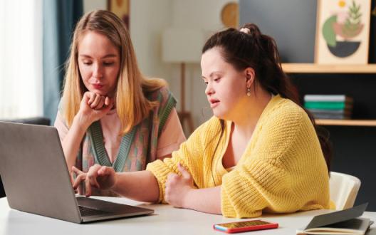 a person with disability sitting at a computer with a support coordinator going over their NDIS plan