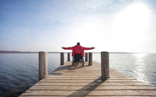 person in a wheelchair at the end of a pier holding his arms out in joy and achievement